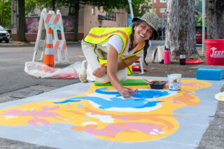 UpStream Art Artist Rae Matagora working on storm drain mural in July 2022